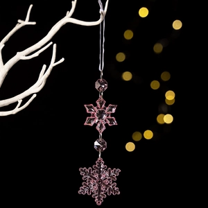 Macro detail of pink acrylic hexagonal snowflake ornament hanging on a white branch