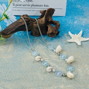 Detailed view of beach shell necklace with blue flower beads on a sandy background