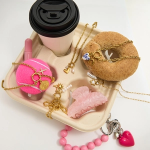 Flat lay of gold pearl necklaces, heart pendants and pink accessories in a coffee tray