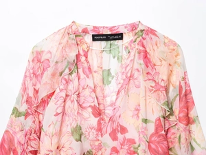 Dettaglio del top in chiffon a fiori rosa con scollo a balze ed etichetta del marchio