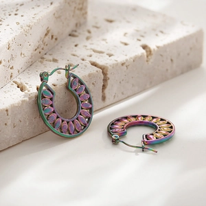 Macro shot of rainbow iridescent hoop earrings with leaf filigree on stone surface