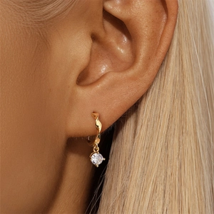 Close-up of golden twisted hoop earrings with a single round clear zircon drop on model