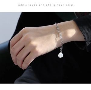 Silver paperclip link bracelet with a round engraved coin pendant worn on a wrist