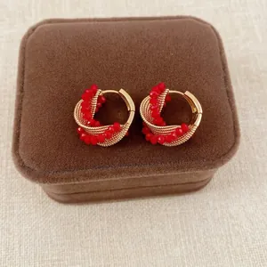 Elegant gold twisted hoop earrings with layered red glass beads on a jewelry box