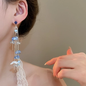 Detail of blue acrylic flower tassel earrings with silver chains on model