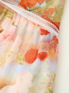 Detail shot of orange floral chiffon fabric with delicate white lace embroidery trim