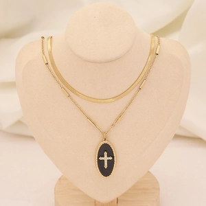 Détail d'un collier doré multicouche avec pendentif croix noire sur un buste beige