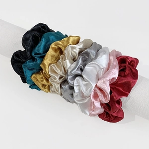 Macro shot of eight colorful satin scrunchies displayed on a minimalist white cylinder stand