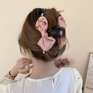 Detail of pink satin bow hair claw with pearl trim shown on an elegant half-up hairstyle