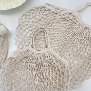 Close-up of two woven hollow fruit mesh bags in beige with wide handles on white surface