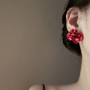 Close-up of model wearing large red floral stud earring with gold center detail