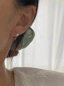 Close-up of a minimalist gold hoop earring with a round pearl on a model's ear