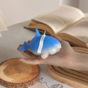 Detailed close-up of a blue and white whale candle held in hand with decorative ribbon