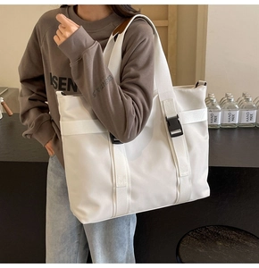 Detail of white canvas tote bag featuring adjustable black buckles and shoulder strap