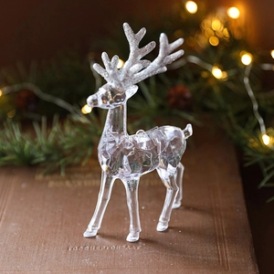 Clear acrylic Christmas reindeer ornament with silver glitter accents on a book background