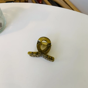 Detailed view of the olive green acrylic hair claw with a unique twisted cross design