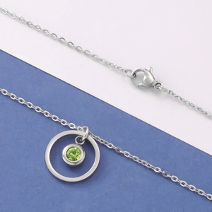 Detail of silver stainless steel necklace with round pendant featuring a green birthstone