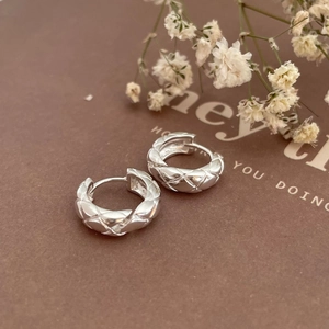 Close-up of S925 sterling silver hoop earrings with quilted diamond texture on brown background