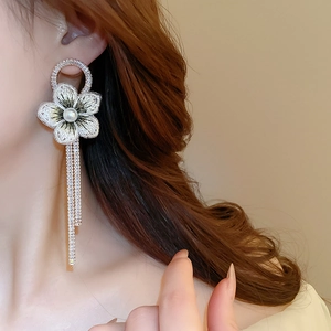 Détail macro de boucle d'oreille fleur brodée blanche avec perle et chaînes à pompons
