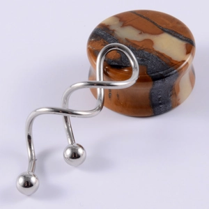 Detailed view of stainless steel spiral barbell piercing and marble pattern stone ear plug