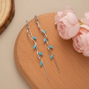Detailed view of silver leaf tassel earrings with blue marquise stones on wood display