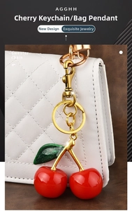 Macro view of a red resin cherry keychain with green glitter leaves on a white quilted bag