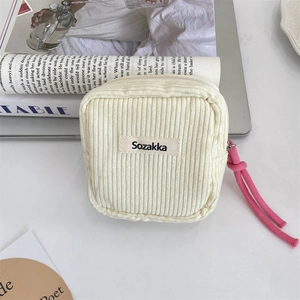 Detail view of cream corduroy cosmetic bag with pink knot zipper and brand label