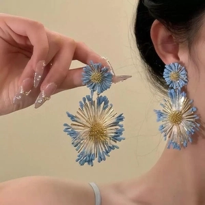 Gros plan de boucles d'oreilles fleurs 3D bleues avec cœur doré sur un mannequin