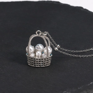 Détail d'un pendentif panier de fleurs argenté avec perles blanches et pierres de zircon