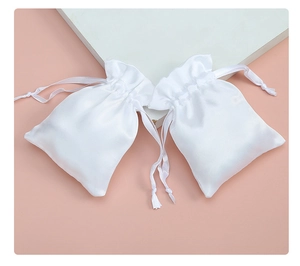 Detail view of white satin drawstring jewelry pouches with silky texture and smooth ribbons