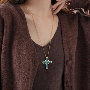 Luxurious gold cross necklace with emerald green gemstones worn on a sweater