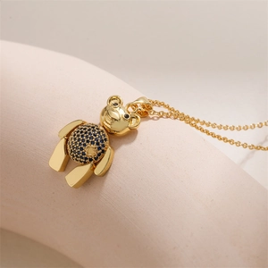 Collier ours doré chic avec zircon bleu et détail cœur sur fond rose poudré élégant