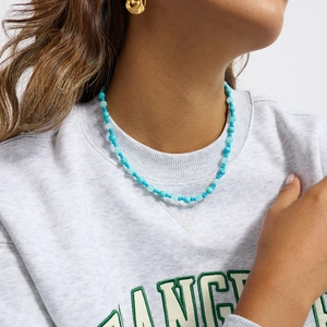 Detail of turquoise and light blue beaded necklace worn on a model against white background