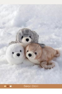 Tre peluche realistici di foca in bianco, grigio e marrone su una superficie innevata