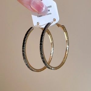 Close-up of gold hoop earrings with black rectangular crystals on a hanging display
