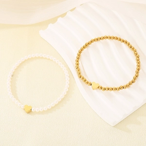 Detail view of gold heart charm bracelets featuring white pearls and golden metal beads.