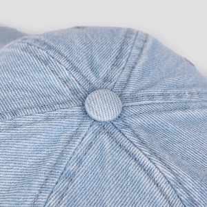 Macro shot of light blue denim baseball cap crown with button and reinforced stitching
