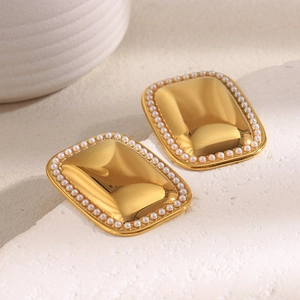 Macro detail of rectangle gold earrings with pearls on white textured background