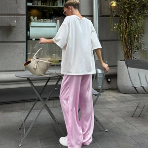 Rückansicht eines Models in rosa Satin-Hose mit weitem Bein in einem stilvollen Straßencafé
