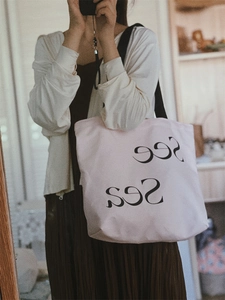 Detail of light pink canvas tote bag with See Sea print and black woven shoulder straps