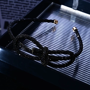 Close-up of a luxury black rhinestone bow bracelet with gold tips on reflective glass
