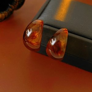 Macro shot of amber resin C-shaped earrings with polished texture on leather surface