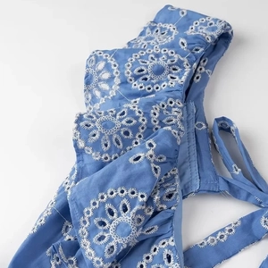Close-up of intricate white eyelet embroidery on a blue midi dress with detailed stitching