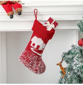 Knitted red Christmas stocking with white house pattern holding a gift box on fireplace