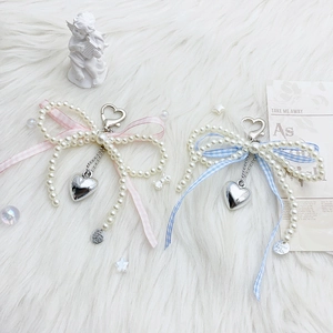 Bow pearl bag charm with silk ribbon and heart pendant on white fur background