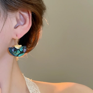 Close-up of shell-texture fan-shaped drop earrings worn by a model in warm light
