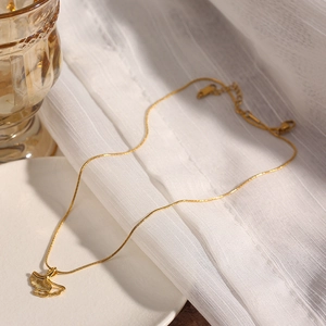 Collana in acciaio al titanio dorato con ciondolo a foglia di ginkgo su un piatto bianco