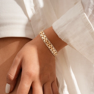 Macro detail of gold watch-style bracelet with pavé rhinestones on a white shirt sleeve