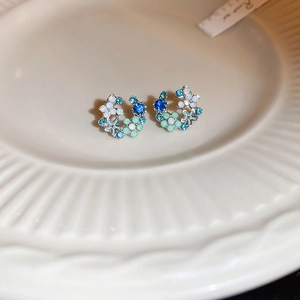 Macro shot of silver C-shaped earrings with blue crystals and enamel flowers detail