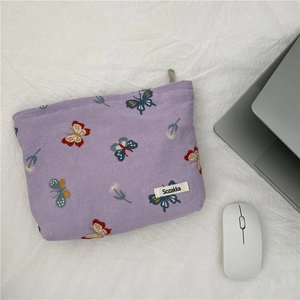Detail of purple fabric makeup bag featuring butterfly embroidery and silver zipper